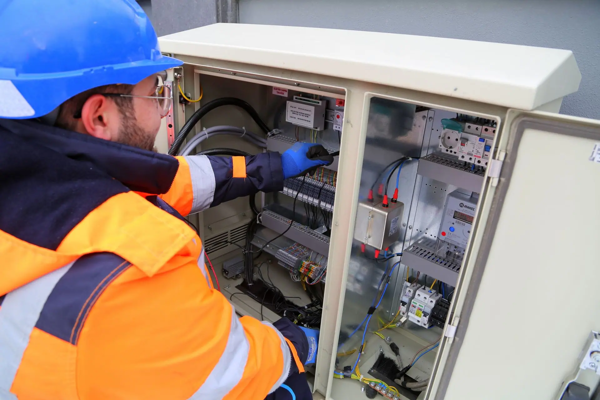 Electrician in a hard hat and safety jacket working on an open commercial electrical panel