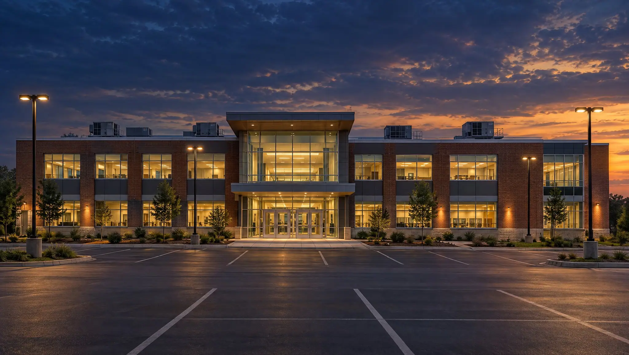 Brick and glass school building with its main entrance lit at dusk.