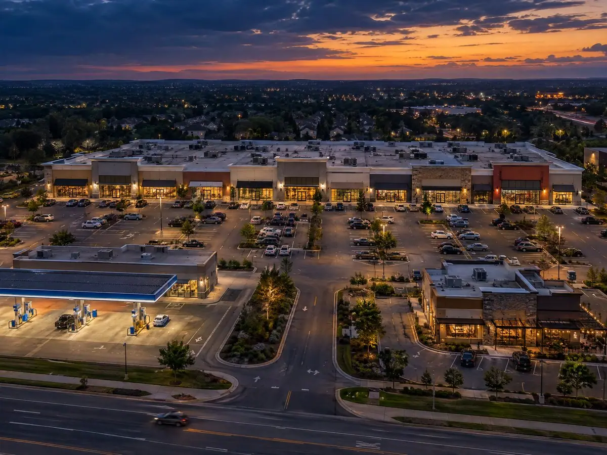 Aerial view of a retail plaza with franchise stores, a fuel station and a parking lot at dusk.